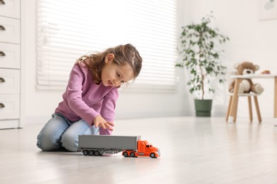 Photo of Little girl playing with toy car on floor at home, space for text