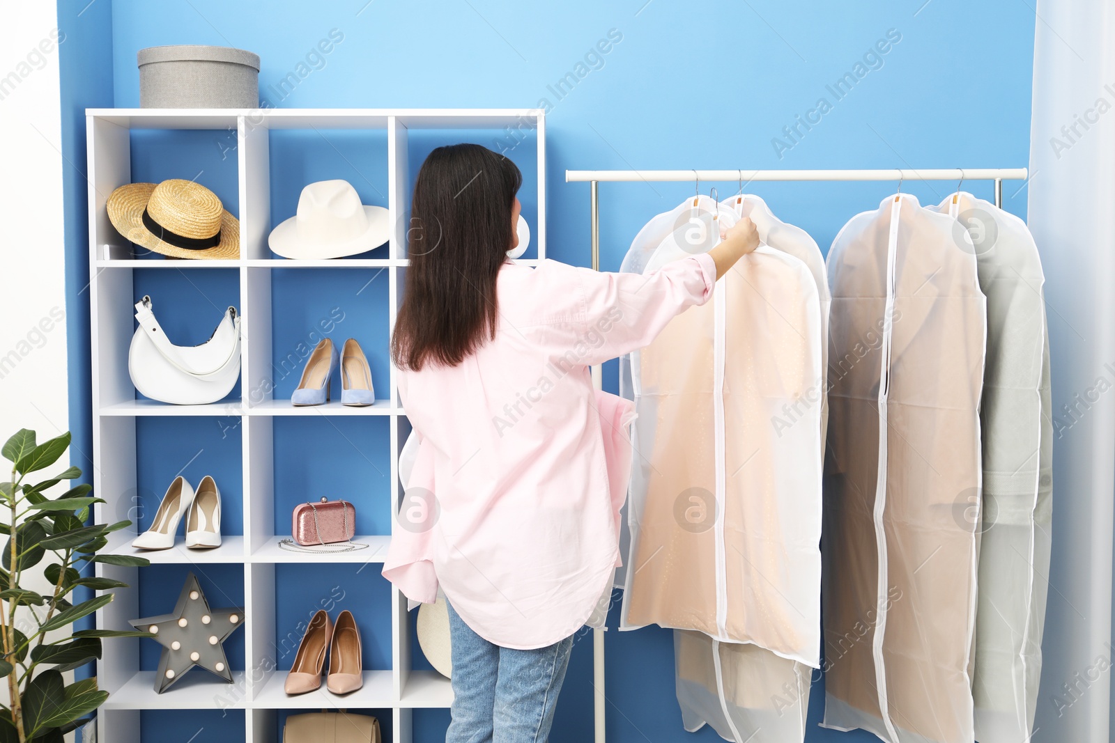 Photo of Woman taking garment cover with clothes from rack indoors