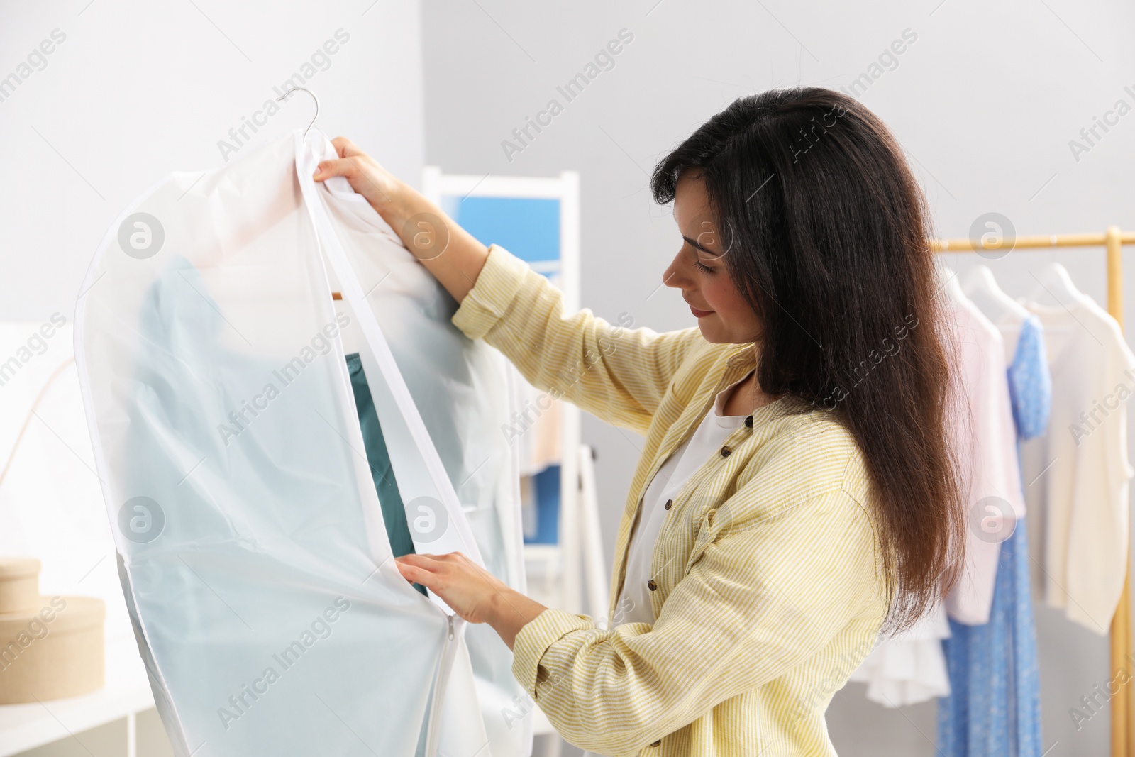 Photo of Woman holding garment cover with clothes indoors