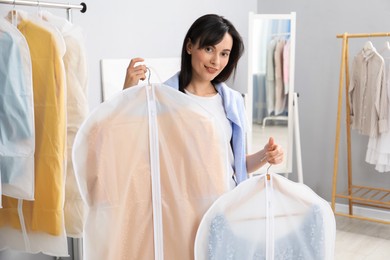 Photo of Woman holding garment covers with clothes indoors