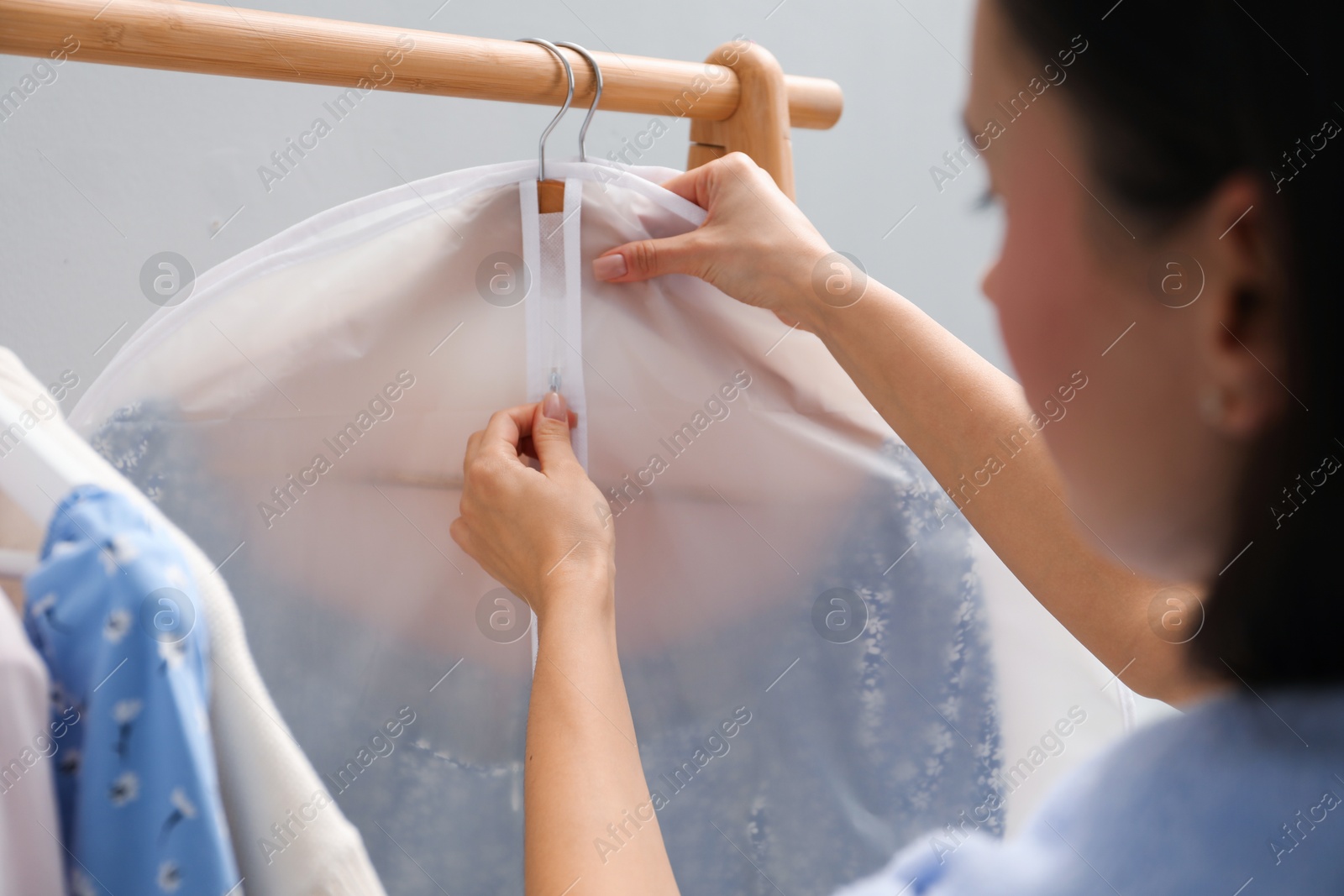 Photo of Woman zipping garment cover with clothes indoors, closeup