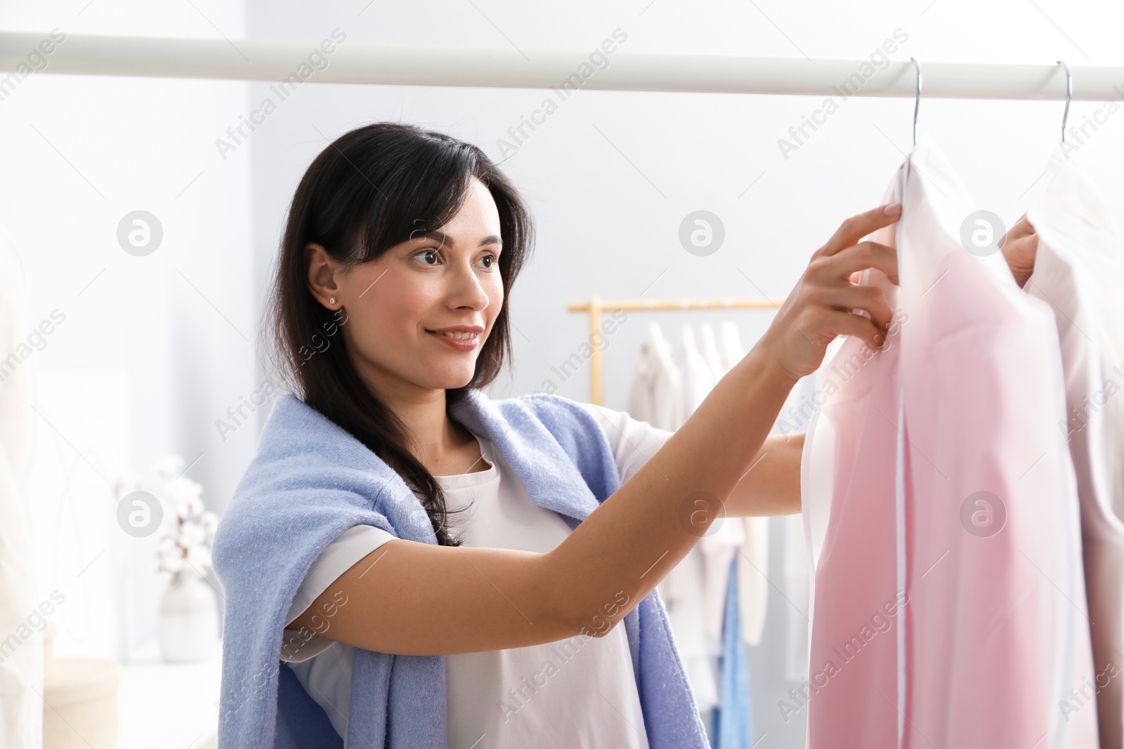 Photo of Woman taking garment cover with clothes from rack indoors