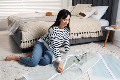 Photo of Woman zipping garment cover with clothes on floor indoors