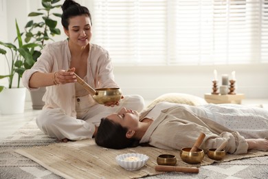 Woman undergoing singing bowl therapy lying on floor indoors. Space for text