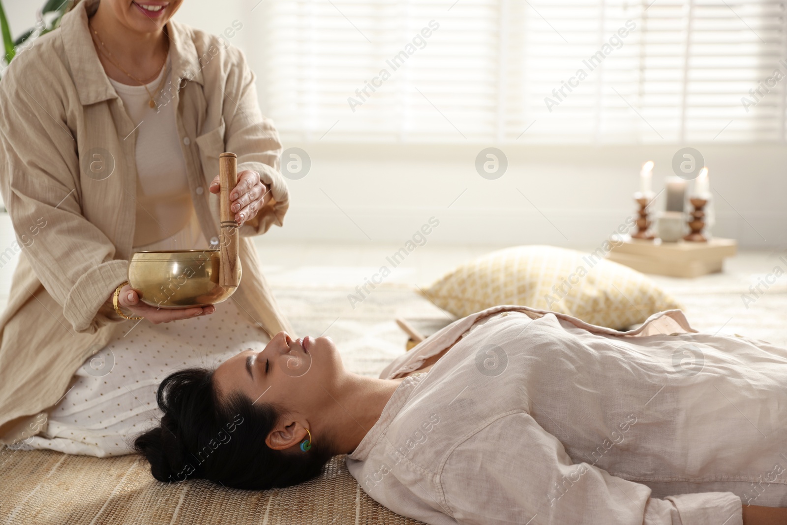 Photo of Woman undergoing singing bowl therapy lying on floor indoors. Space for text