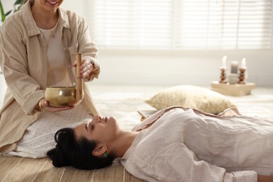 Woman undergoing singing bowl therapy lying on floor indoors. Space for text