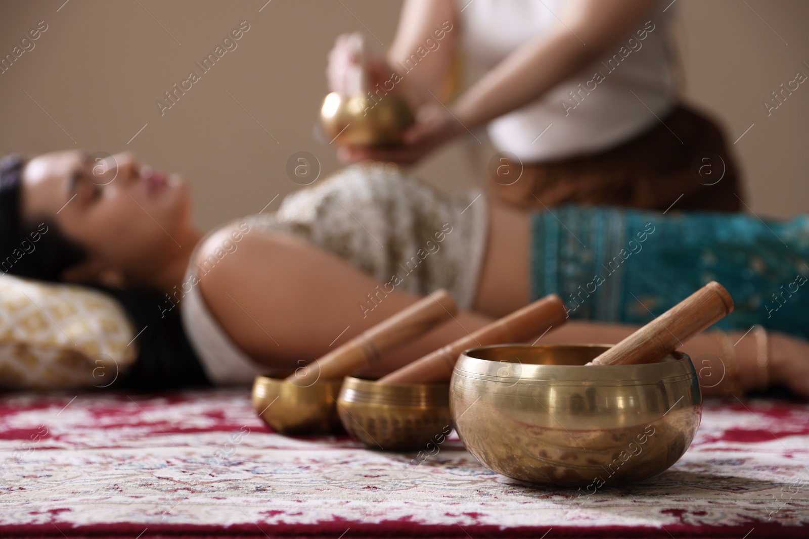 Photo of Woman undergoing singing bowl therapy indoors, selective focus