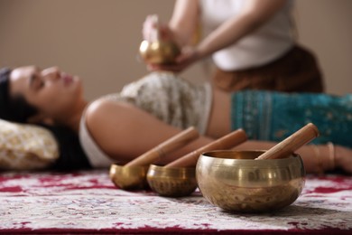 Photo of Woman undergoing singing bowl therapy indoors, selective focus