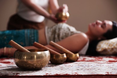 Photo of Woman undergoing singing bowl therapy indoors, selective focus