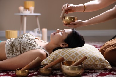 Woman undergoing singing bowl therapy lying on floor indoors