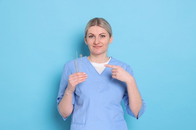 Photo of Professional dentist pointing at tools on light blue background