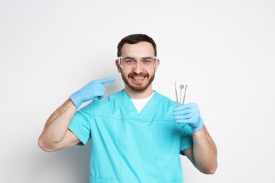 Photo of Professional dentist with tools pointing at his smile on light background