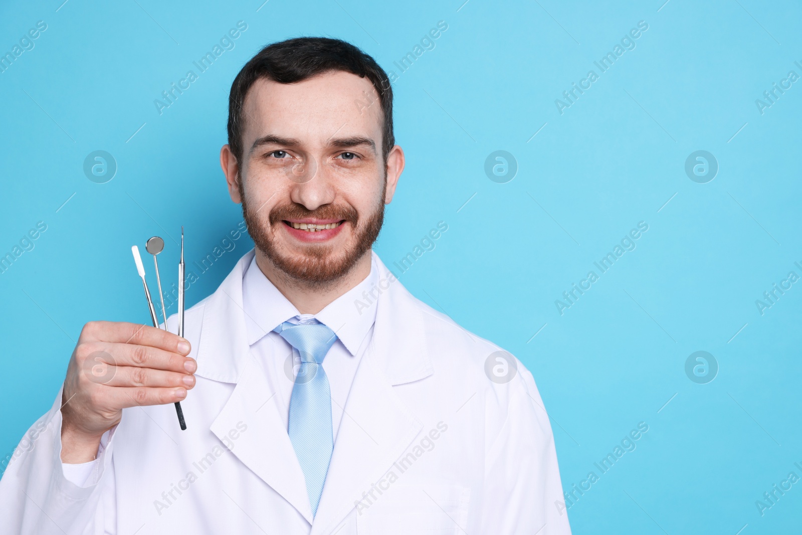 Photo of Professional dentist with tools on light blue background. Space for text