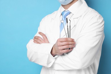 Professional dentist with tools on light blue background, closeup