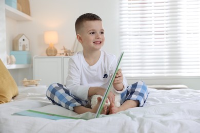 Photo of Bedtime. Cute boy with toy sheep reading book on bed indoors