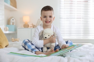 Photo of Bedtime. Cute boy with toy sheep reading book on bed indoors