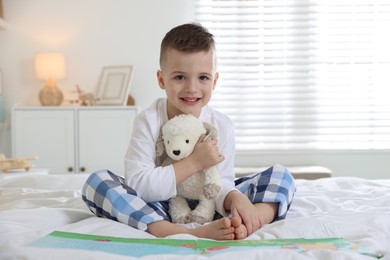 Photo of Bedtime. Cute boy with toy sheep reading book on bed indoors