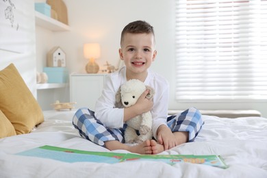 Photo of Bedtime. Cute boy with toy sheep reading book on bed indoors