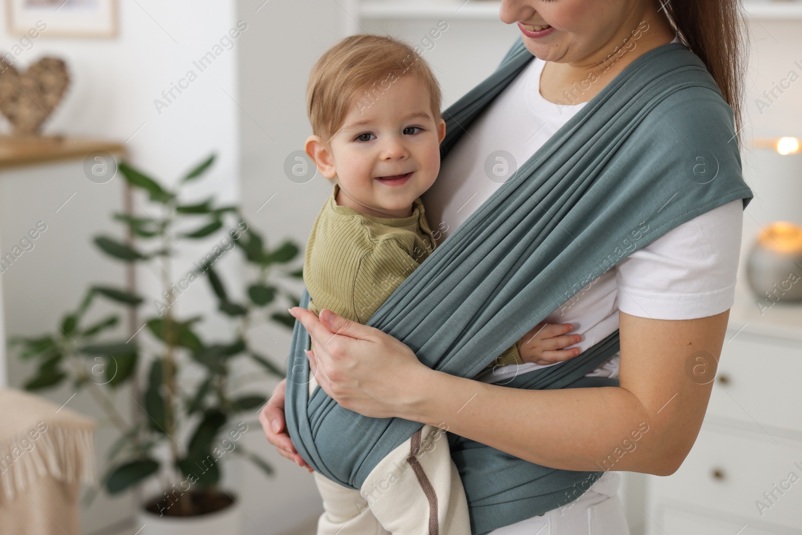 Photo of Mother holding her child in sling (baby carrier) at home, closeup. Space for text