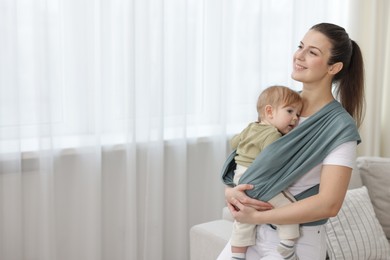 Photo of Mother holding her child in sling (baby carrier) at home, space for text