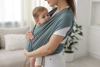 Mother holding her child in sling (baby carrier) at home, closeup