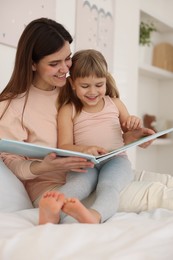 Photo of Bedtime. Happy little daughter reading book with her mother on bed at home