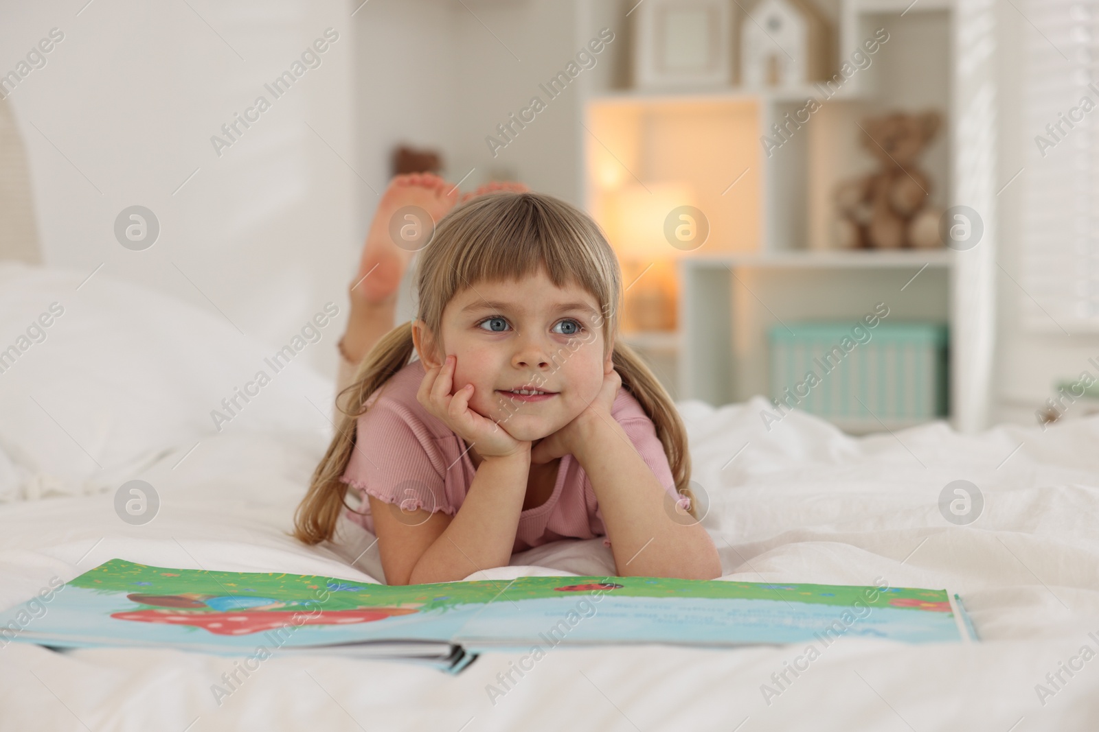 Photo of Bedtime. Happy little girl with book lying on bed at home