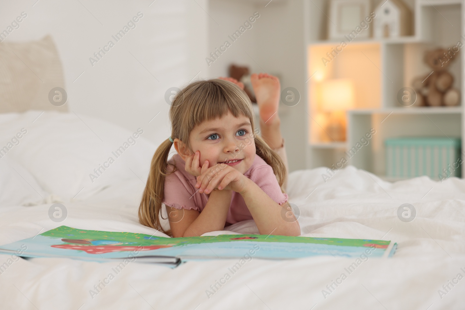 Photo of Bedtime. Happy little girl with book lying on bed at home