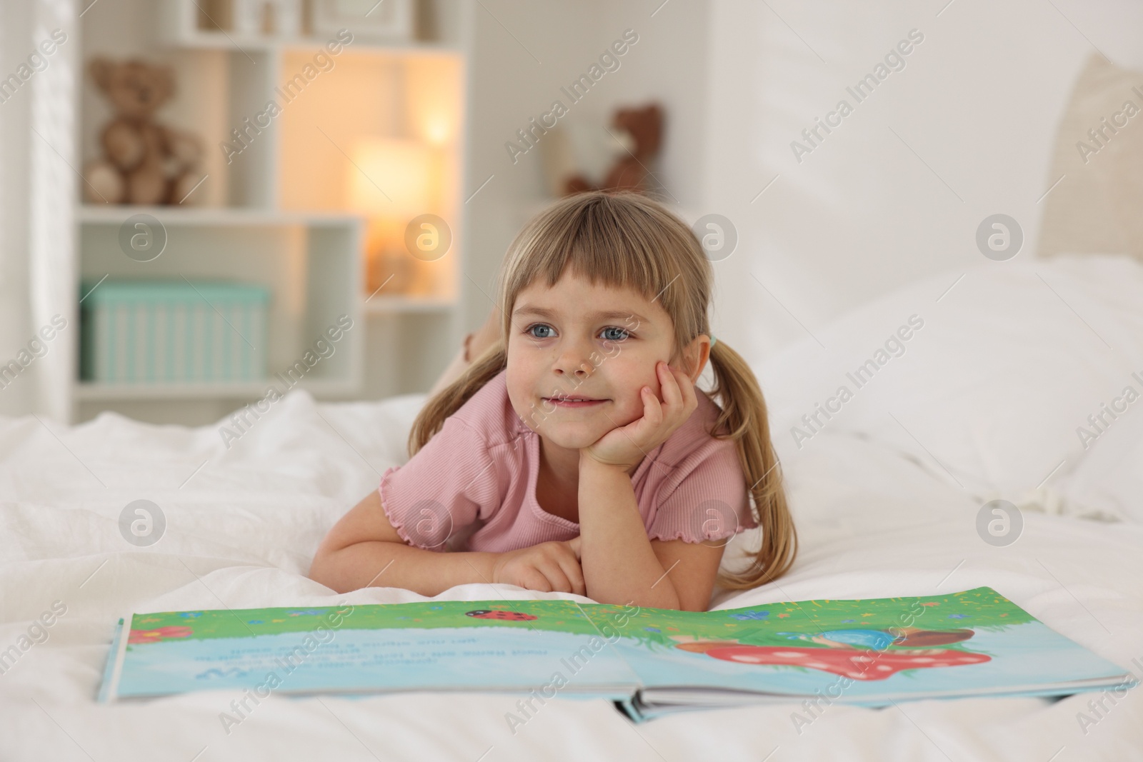 Photo of Bedtime. Cute little girl with book lying on bed at home