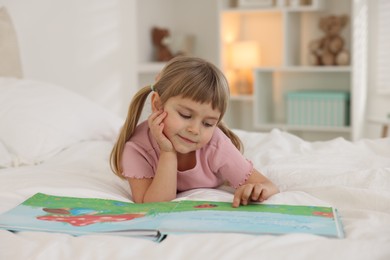 Bedtime. Cute little girl reading book on bed at home