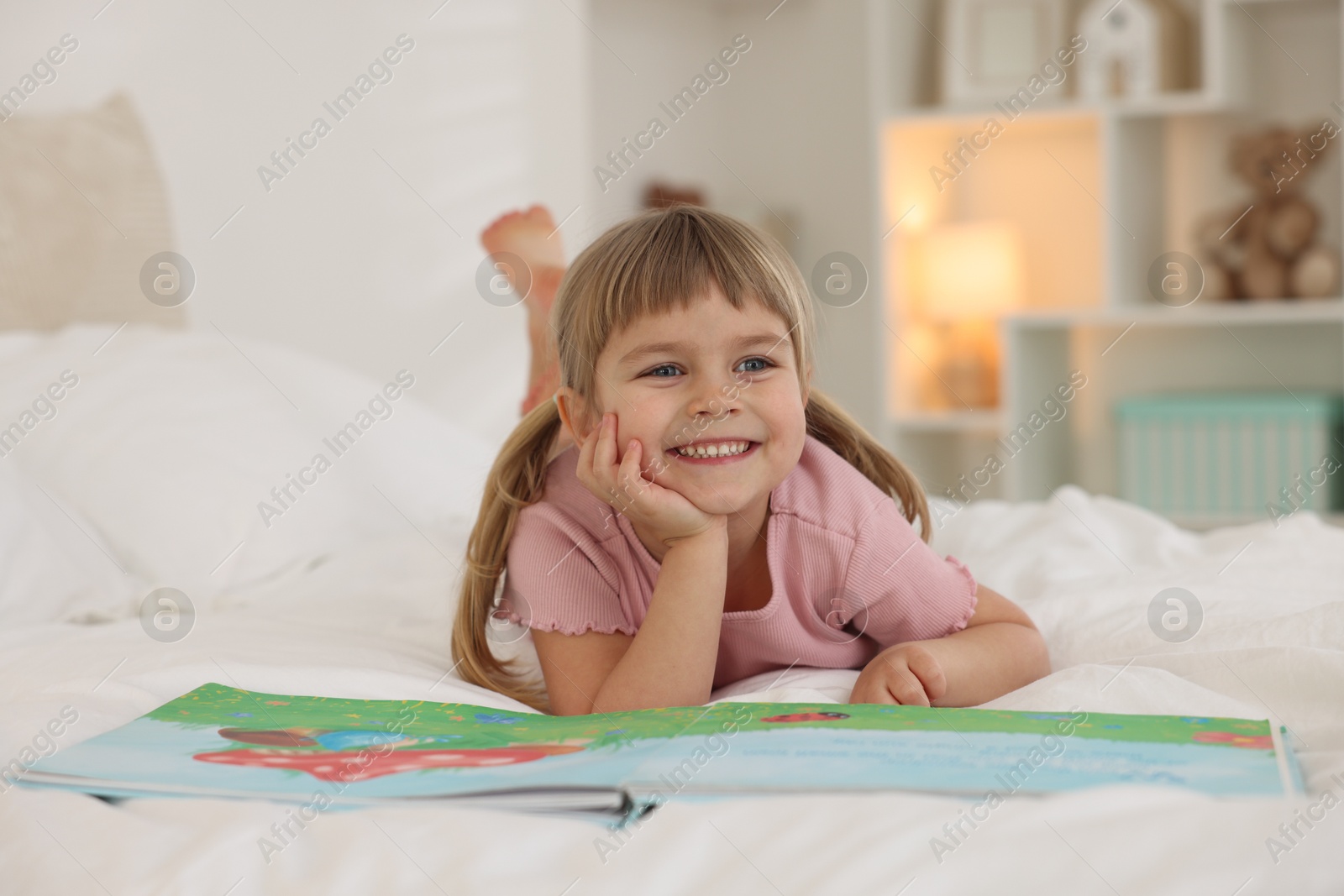 Photo of Bedtime. Happy little girl with book lying on bed at home