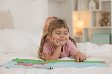 Photo of Bedtime. Happy little girl reading book on bed at home