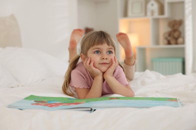 Photo of Bedtime. Cute little girl with book lying on bed at home