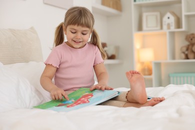 Photo of Bedtime. Happy little girl with book sitting on bed at home