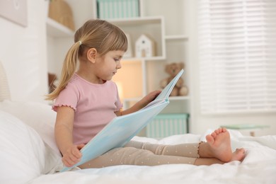 Photo of Bedtime. Cute little girl with book sitting on bed at home