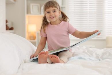 Photo of Bedtime. Happy little girl with book sitting on bed at home