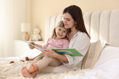 Photo of Bedtime. Happy little daughter reading book with her mother on bed at home