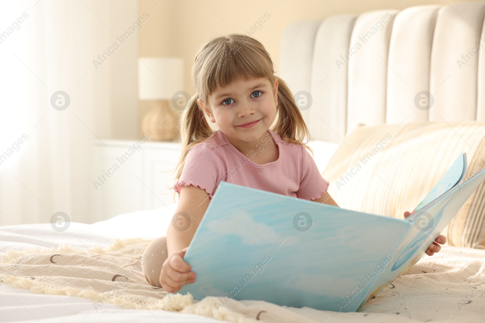 Photo of Bedtime. Cute little girl reading book on bed at home