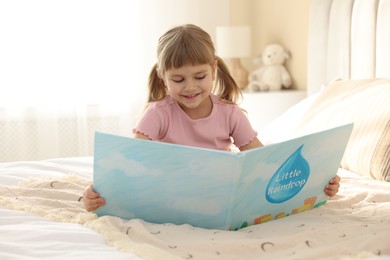 Photo of Bedtime. Happy little girl reading book on bed at home