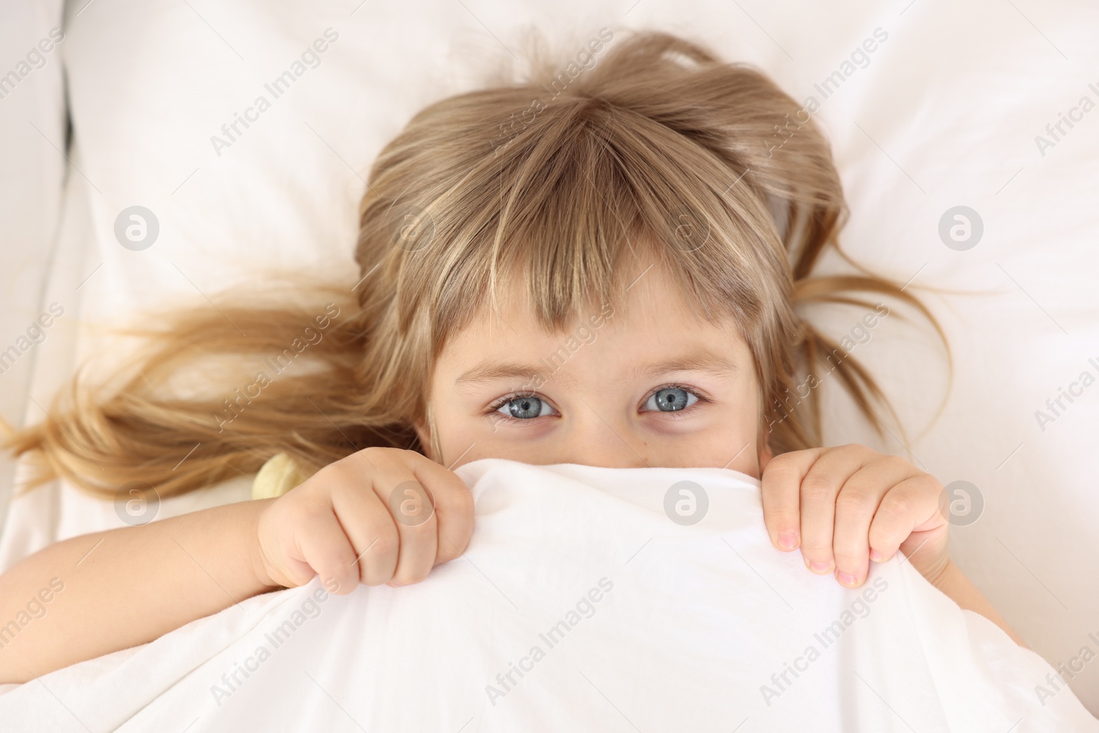 Photo of Bedtime. Cute little girl covering mouth with blanket in bed, top view