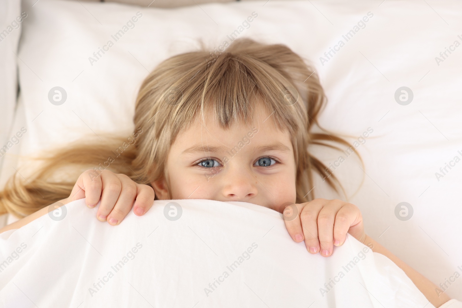 Photo of Bedtime. Cute little girl covering mouth with blanket in bed, top view