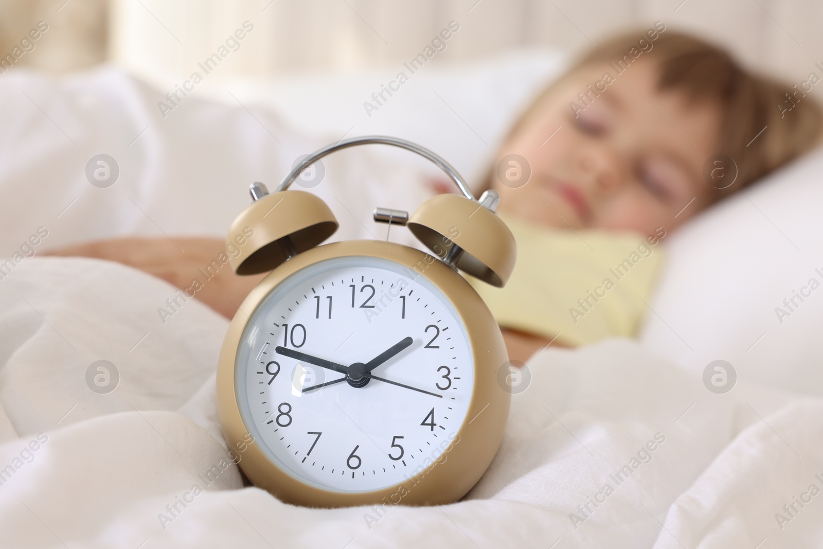 Photo of Bedtime. Cute little girl sleeping in bed, focus on alarm clock