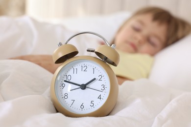 Bedtime. Cute little girl sleeping in bed, focus on alarm clock