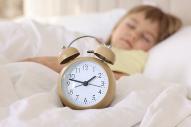 Photo of Bedtime. Cute little girl sleeping in bed, focus on alarm clock