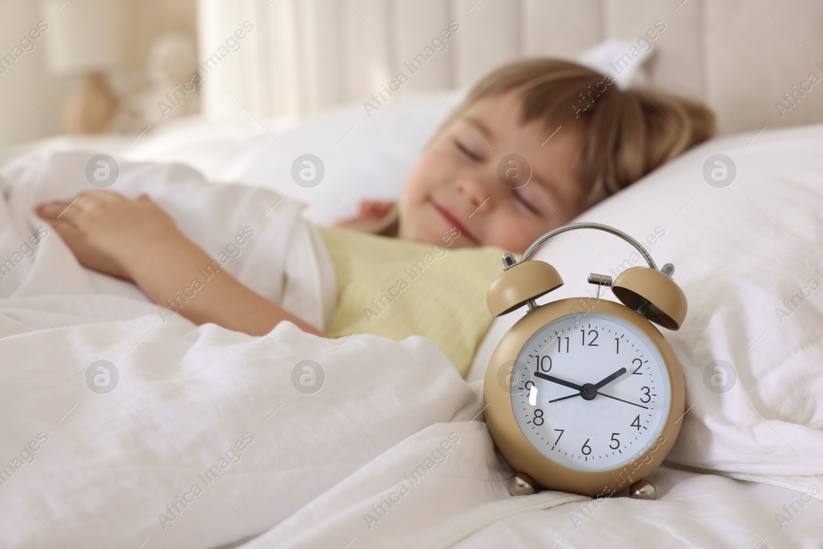 Photo of Bedtime. Cute little girl sleeping in bed, focus on alarm clock