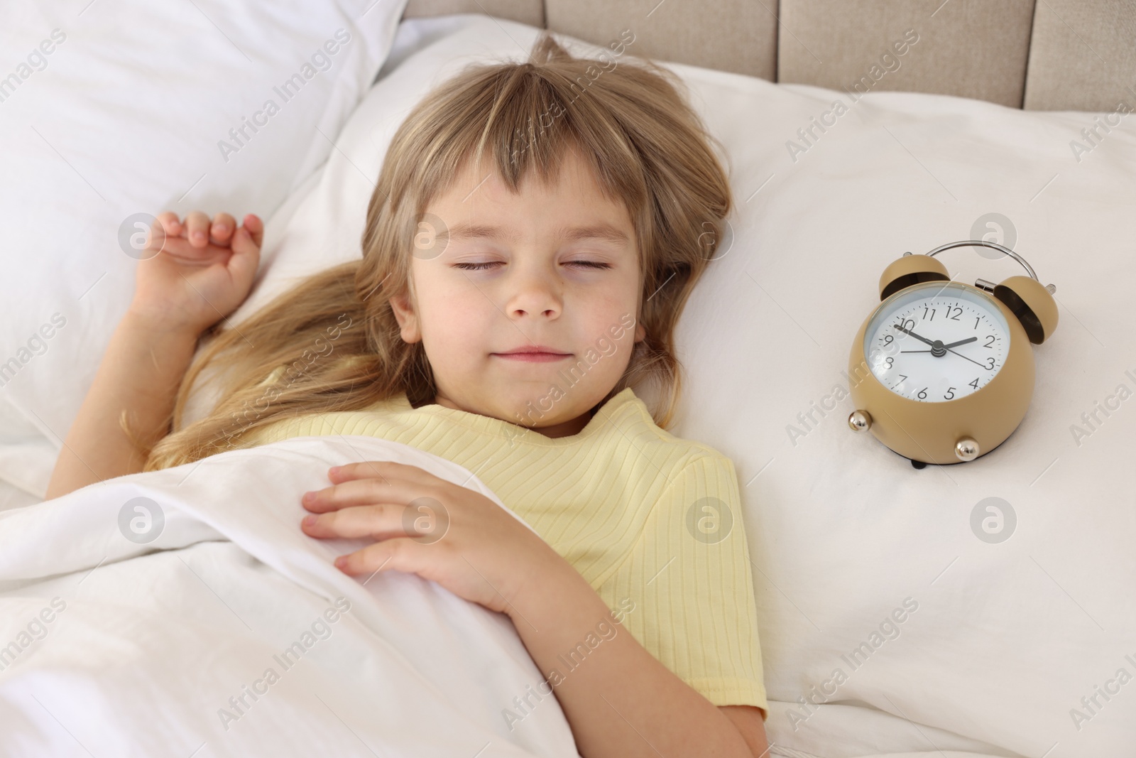 Photo of Bedtime. Cute little girl sleeping with alarm clock in bed