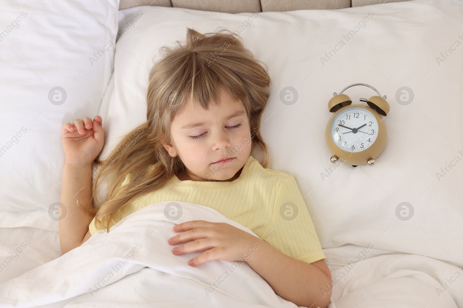 Photo of Bedtime. Cute little girl sleeping with alarm clock in bed