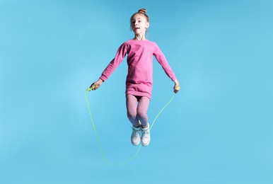 Photo of Cute little girl with jump rope on light blue background