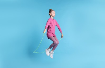 Cute little girl with jump rope on light blue background