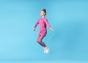 Cute little girl with jump rope on light blue background